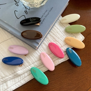 Set mit 10 bunten ovalen Macaron-Haarspangen mit Goldlabel auf einem Holzhintergrund