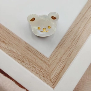 Detail view of a white acetate bear hair clip with golden facial accents and pearly finish