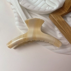 Détail macro d'une grande pince à cheveux en acétate marbré crème sur tissu blanc