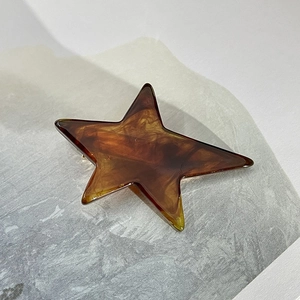 Macro view of the amber tortoiseshell star-shaped hair clip on a marble surface