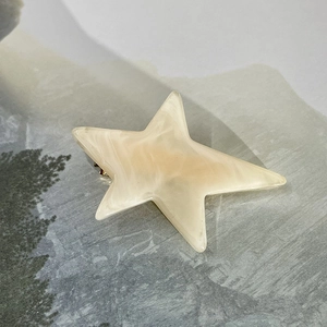 Detail of star-shaped acetate hair clip with cream marble texture and metal duckbill grip