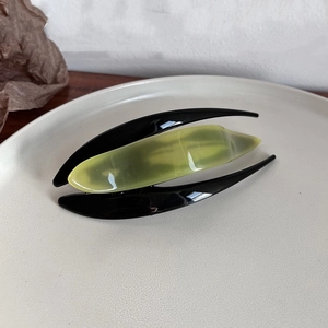 Detail of minimalist green and black acetate hair clip on a ceramic tray display