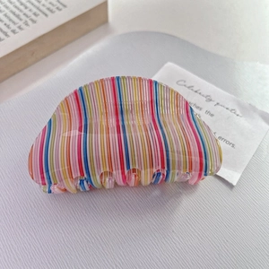 Detail of colorful rainbow striped acetate claw clip on a minimalist white texture background