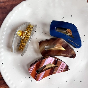 Elegant acetate hair claws in marble patterns set on a white ceramic tray display