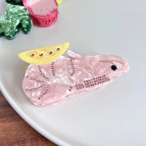 Macro di una molletta per capelli in acetato rosa a forma di gamberetto con strass e limone