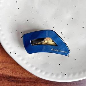 Close-up of a blue acetate hair claw with gold accents on a white decorative plate