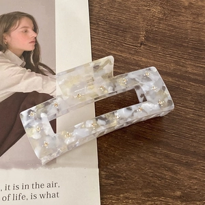 Detailed top view of large rectangular acetate hair claw with marble pattern and gold stars