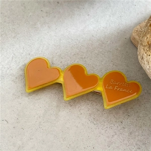 Dettaglio macro di tre fermagli a cuore in resina ambra con scritta Barrette La France