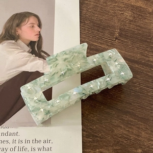Green marble acetate hair claw clip with floral rhinestones on a wooden desk background