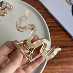 Detailed close-up of M-shaped acetate hair claw with golden metal base and marble texture