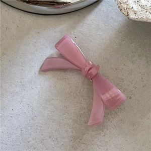 Détail d'une pince à cheveux rose en acétate avec inscription dorée sur fond de pierre