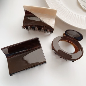Detailed close-up of dark brown and beige acetate hair claws on a ceramic plate