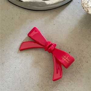 Détail d'une pince à cheveux nœud en acétate rose avec logo doré sur marbre