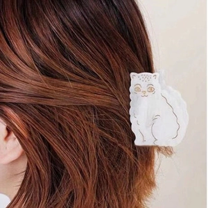 Pince à cheveux chat blanc avec bordure dorée sur cheveux brun foncé sous lumière naturelle