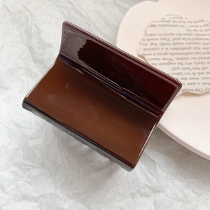 Detailed view of large dark brown acetate hair claw clip on a minimalist aesthetic background