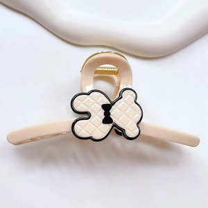 Detail of beige acetate hair claw featuring a quilted pattern bear with a black bow