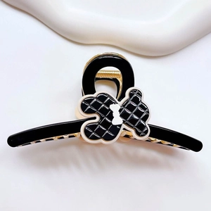 Detail view of a black acetic acid bear hair claw clip with a white bow and textured design