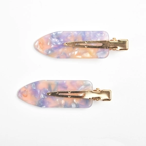 Detail view of two marble patterned acetate hair clips with golden metal duckbill clips