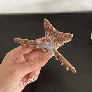 Gros plan d'une pince à cheveux en forme de queue de poisson avec motif marbré marron