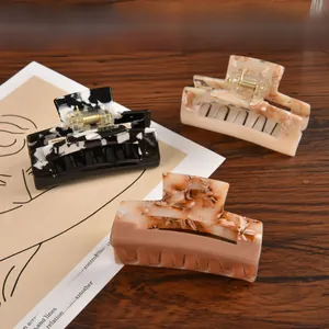 Detail view of large marble pattern hair claws in black, pink and brown on wooden surface