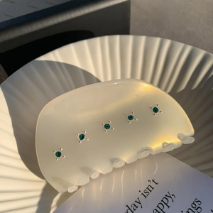 Dettaglio molletta per capelli in acetato crema con strass verdi in una ciotola di ceramica