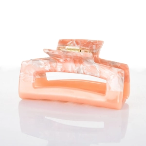 Detailed macro view of acetate hair claw clip showing orange marble texture and metal spring