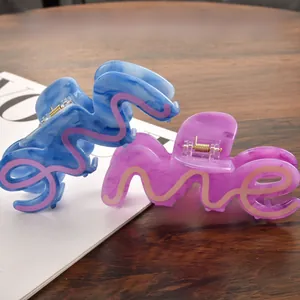 Detail of large acetate hair claws with marble texture and wavy letter design