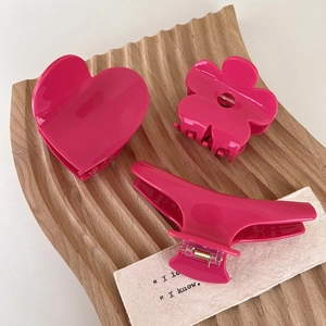 Detailed view of three glossy pink acetic acid hair claws in heart and flower shapes