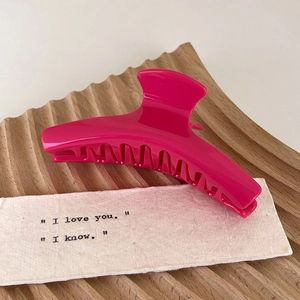 Close-up of a rose red acetate flower hair claw clip on a textured wooden tray