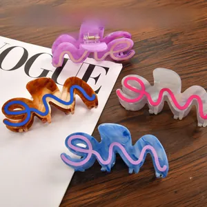 Set of four large colorful wavy hair claws in purple and pearl white on a wooden table
