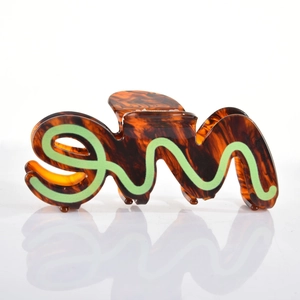 Detailed view of tortoise shell acetate hair claw with neon green wave lettering on white background