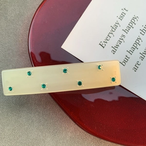 Détail de la pince à cheveux crème avec strass vert émeraude sur décor élégant