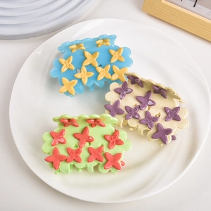 Three acetate flower claw clips in blue, purple and green displayed on a ceramic plate
