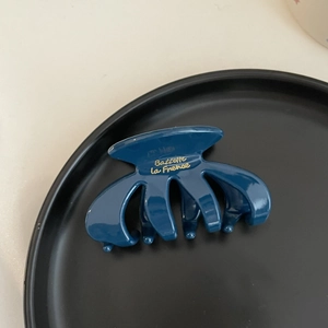 Close-up of a small vintage acetate hair claw clip in dark blue with golden text