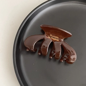Close-up of dark brown acetate hair claw clip with gold lettering on a black tray