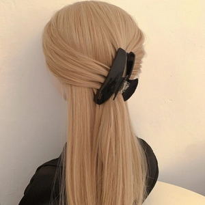 Scallop acetate hair claw clip in black with gold label on model's long blonde hair