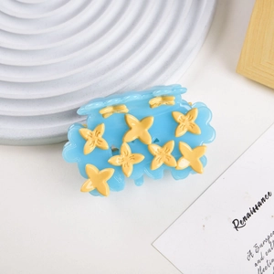 Detail of blue acetate hair claw clip featuring yellow flower motifs on white desktop