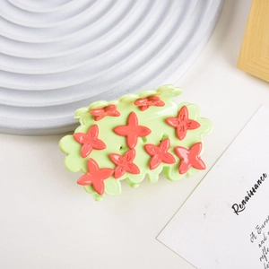 Close-up of green acetate hair claw with red floral accents on a textured display tray