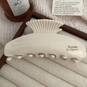 Detail of a beige scallop hair claw clip with gold lettering on a display tray