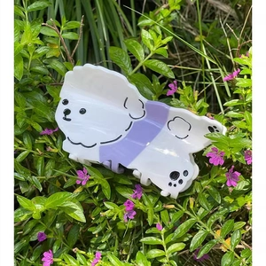 Detailansicht einer weißen Pudel-Haarklammer mit lila Latzhose auf floralem Hintergrund