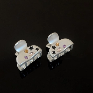 Pair of star-shaped alloy mini hair claws with colorful zircon inlay on a reflective surface