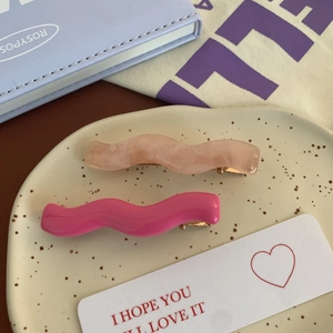 Détail de pinces à cheveux ondulées en marbre orange et rose sur une assiette en céramique