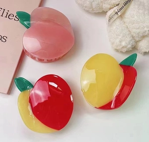 Dettaglio di tre simpatiche mollette per capelli in acetato con disegni di pesca e mango