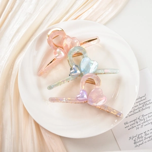 Close-up of three pearlescent heart hair claws in pink, blue and purple on a ceramic plate