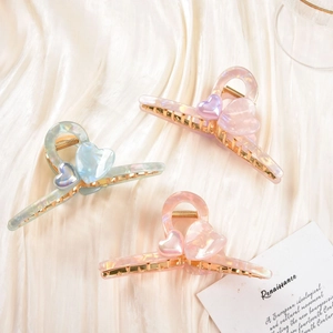 Detail shot of acetate hair claws with metallic teeth and 3D heart motifs in pearly tones