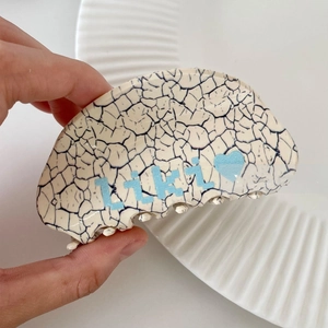Detailed close-up of marble pattern hair claw clip with Likly heart logo held in hand