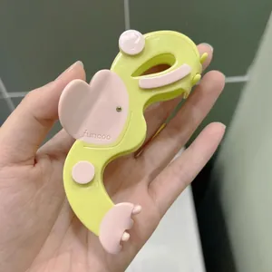 Pince à cheveux cœur en acétate vert et rose avec strass tenue dans la main