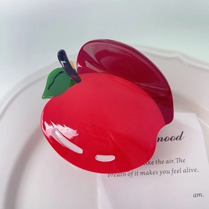 Détail d'une pince à cheveux pomme rouge en acétate brillant sur un plateau blanc