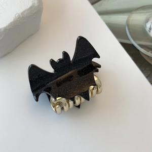 Detail of bat-shaped hair claw clip with black glitter finish and gold metal teeth