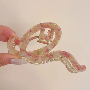 Detail einer großen Haarklammer aus marmoriertem Acetat in Rosa und Gelb mit Goldfeder